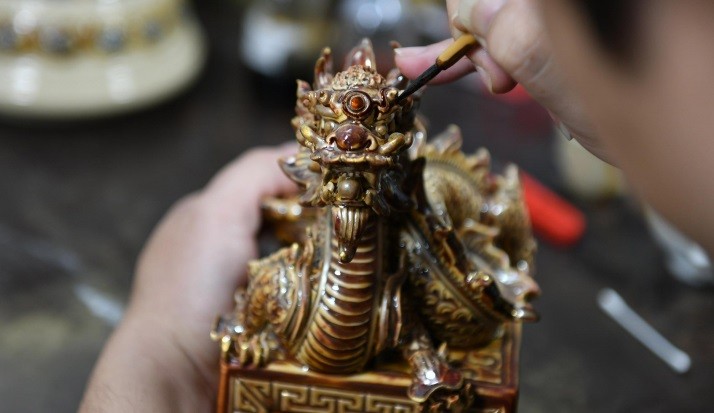 Sản phẩm sau khi ra khỏi lò nung sẽ đi tới công đoạn được chờ đợi nhất là vẽ vàng. Người thợ thủ công sẽ sử dụng vàng pha dạng lỏng đi từng đường nét trên sản phẩm rồng, sau đó sẽ tiếp tục nung từ 6 đến 8 tiếng đồng hồ nữa để có được độ nổi bật, sang trọng. Sản phẩm sau khi ra khỏi lò nung sẽ đi tới công đoạn được chờ đợi nhất là vẽ vàng. Người thợ thủ công sẽ sử dụng vàng pha dạng lỏng đi từng đường nét trên sản phẩm rồng, sau đó sẽ tiếp tục nung từ 6 đến 8 tiếng đồng hồ nữa để có được độ nổi bật, sang trọng.