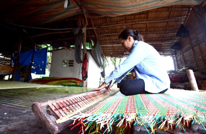 Người phụ nữ ở làng nghề dệt chiếu truyền thống Ngan Dừa  thoăn thoắt chuồi, sắp xếp từng sợi lác theo từng màu vào go khi dệt chiếu.