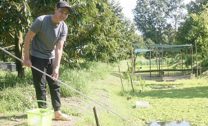 Anh Bùi Hoàng Hồng Thái bên ao vườn nuôi ốc bươu đen của gia đình.