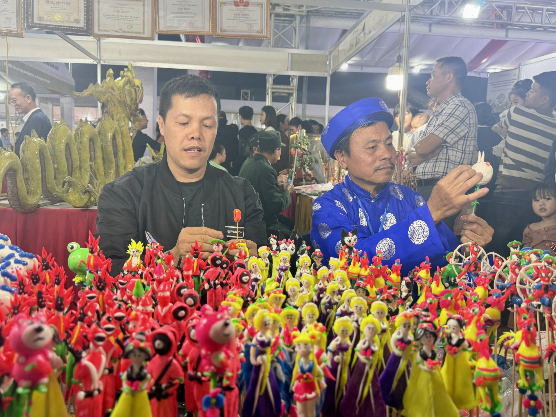 Nghệ nhân Ưu tú Đặng Văn Tiên (bên trái) đang thao diễn nghề nặn tò he tại Triển lãm. Nghệ nhân Ưu tú Đặng Văn Tiên (bên trái) đang thao diễn nghề nặn tò he tại Triển lãm.