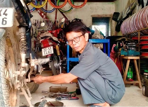 Ông Nguyễn Việt Hùng đang sửa chữa xe máy cho khách Ông Nguyễn Việt Hùng đang sửa chữa xe máy cho khách